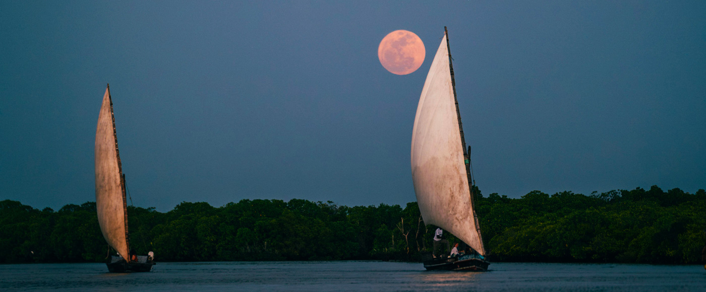 bateaux traditionnels dhow naviguant de nuit sous la pleine lune au large de Lamu au Kenya